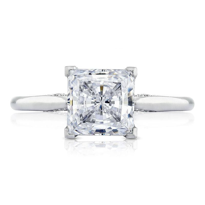 A close-up of the Tacori Classic Crescent RoyalT engagement ring showcases a princess-cut diamond in a prong setting, designed by Tacori artisans. This stunning piece features an intricate geometric design on an 18K white gold band with diamond accents, perfectly highlighting its elegant simplicity.