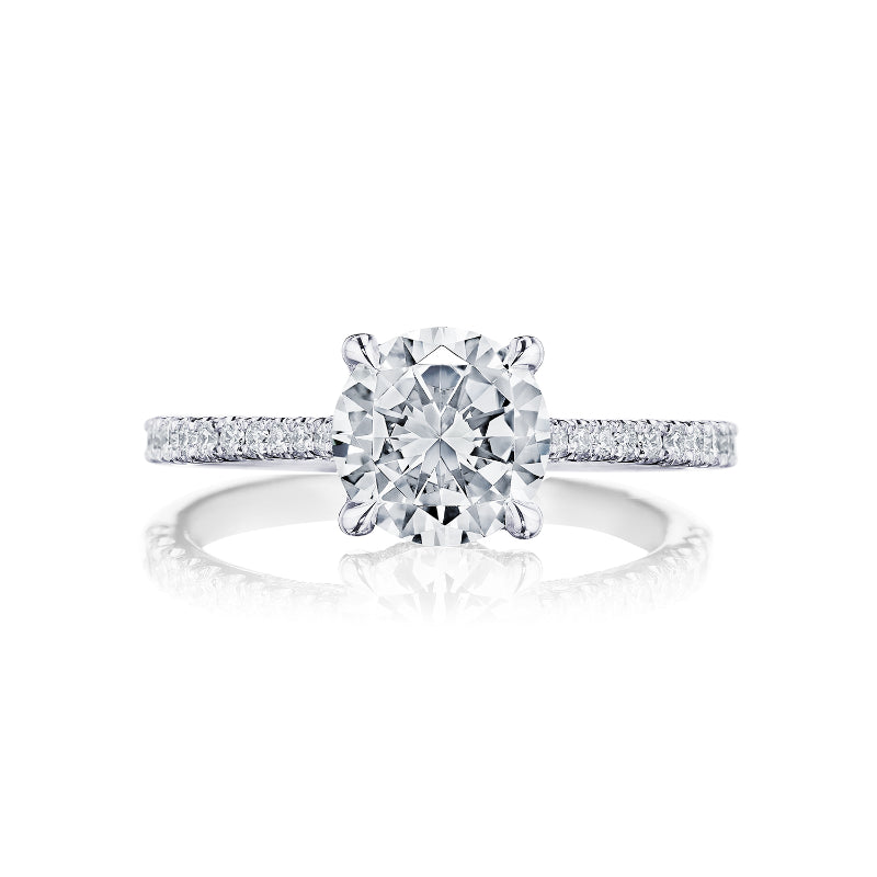 A close-up image of the Tacori Simply Tacori Platinum Round Brilliant Semi Mount with Diamond Band and Hidden Halo Engagement Ring showcases a large round diamond in the center, secured by four prongs. The band, adorned with small diamonds, enhances its elegance and sparkle, while the signature TACORI crescent adds a distinctive touch to this exquisite masterpiece.