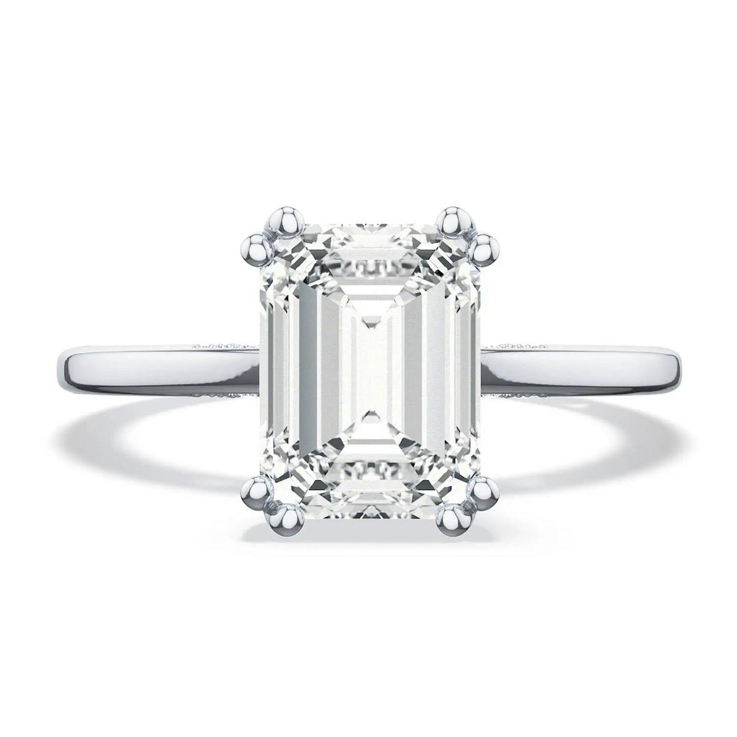 A close-up image of the Tacori Simply 18K White Gold Emerald Solitaire Semi Mount Engagement Ring, crafted by TACORI experts, features a large emerald-cut diamond set with four prongs. The elegant band displays the Signature Crescent design and diamond accents, enhancing the beauty of the central gemstone as it reflects light through its stunning facets.