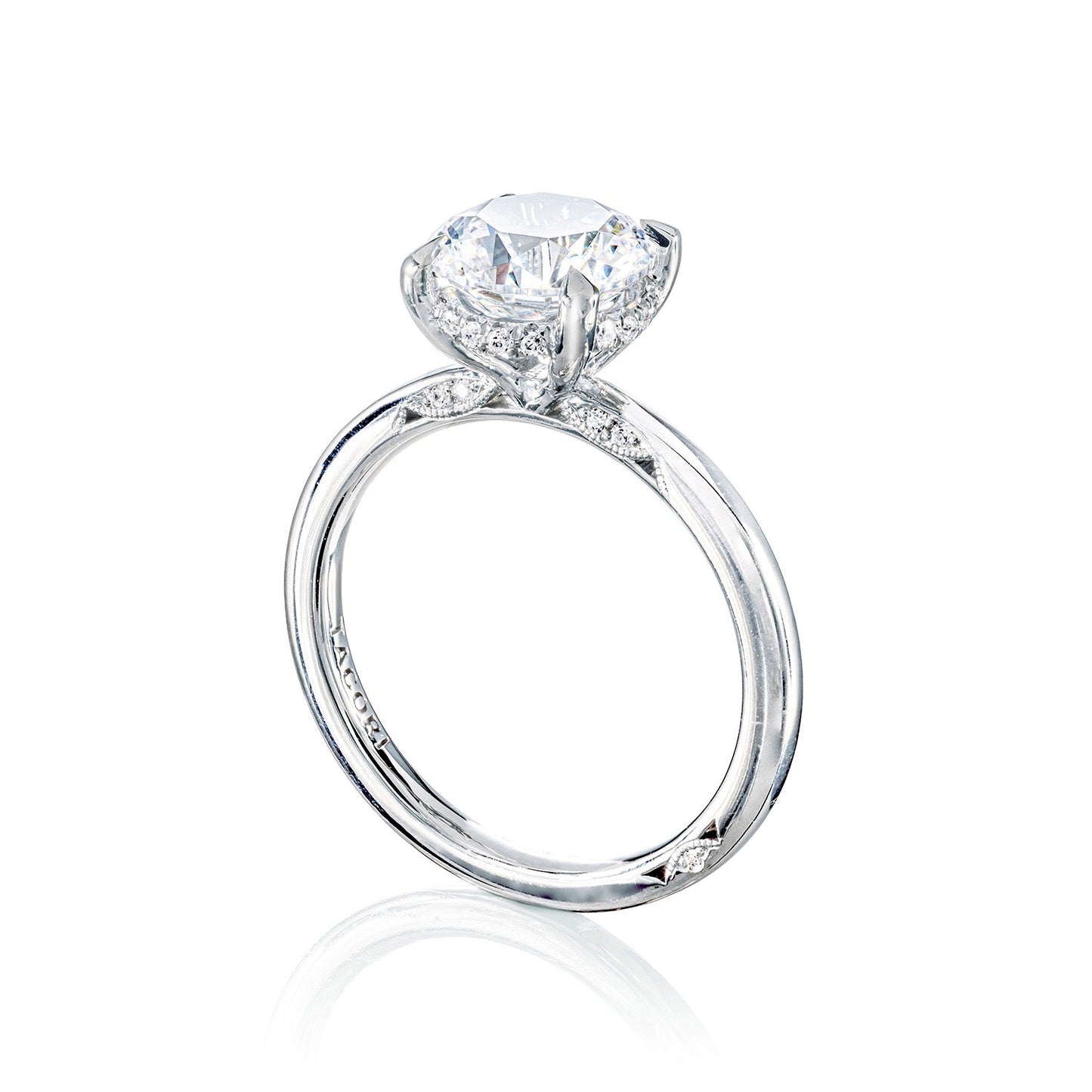 The Tacori Simply 18K White Gold Round Brilliant Solitaire Semi Mount Engagement Ring, featuring a stunning round diamond centerpiece, is complemented by a band with subtle diamond accents. Presented on a reflective surface against a white backdrop, this refined piece embodies timeless elegance and the lasting allure of diamonds.