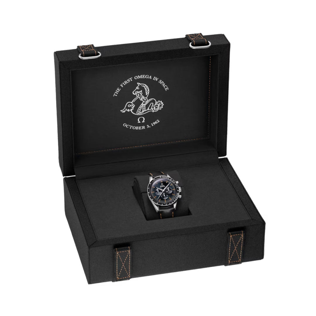 An OMEGA Speedmaster First OMEGA in Space Co-Axial Master Chronometer 39.7mm Watch by OMEGA sits in an open black case with white stitching. The lid displays a graphic and the text, "The First Omega in Space, October 3, 1962.