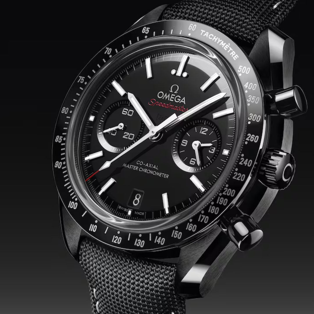 Close-up of the OMEGA Speedmaster Dark Side of the Moon Co-Axial Master Chronometer 44.25mm watch featuring a fabric strap, three sub-dials, tachymeter bezel, and chronograph pushers against a dark gradient background.
