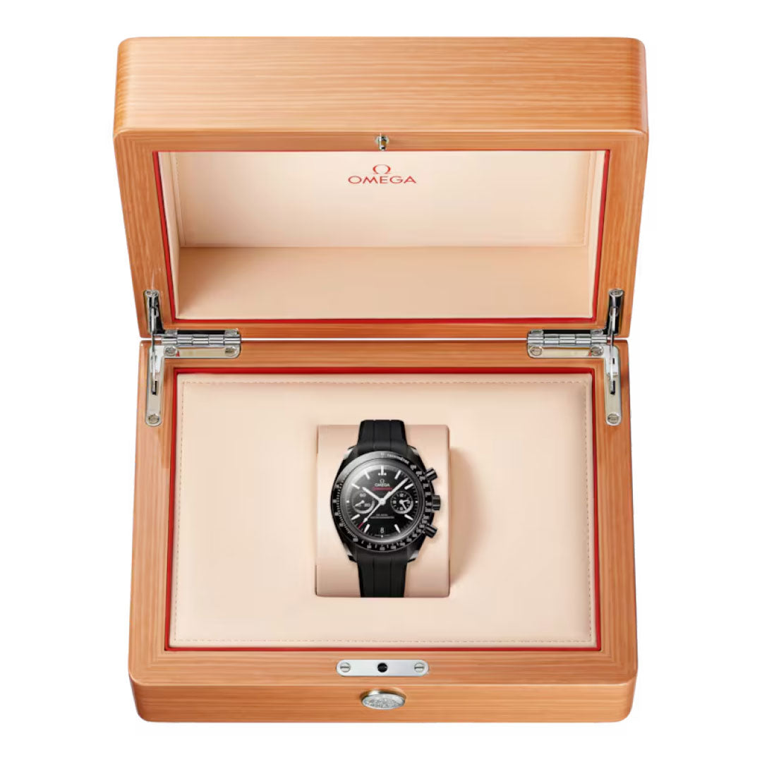 An OMEGA Speedmaster Dark Side of the Moon Co-Axial Master Chronometer 44.25mm watch with a black ceramic case and strap, shown in an open light wooden OMEGA box featuring a cream and beige interior.