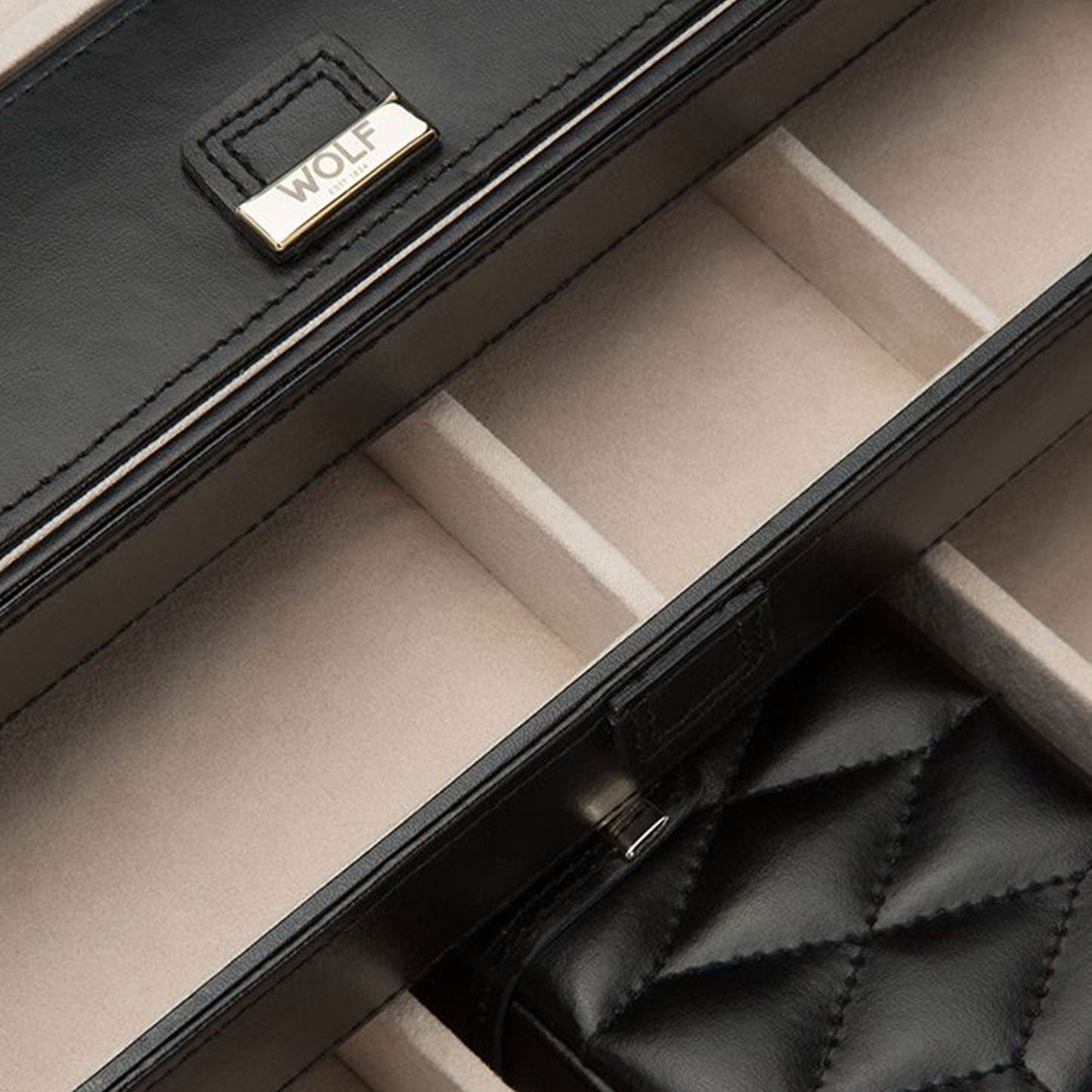 The WOLF 1834 Caroline Black Jewellery Box is a luxurious piece crafted from diamond-quilted black leather. Its interior features a beige lining with LusterLocâ„¢ technology and multiple sections for organizing your jewelry. The box also includes a metal label inscribed with "WOLF.