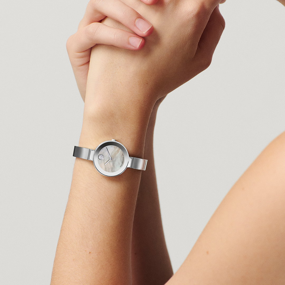 A silver-tone Movado BOLD Bangle Quartz 28mm Watch with a mother-of-pearl dial and a single dot marker at the twelve o’clock position, worn on a wrist.