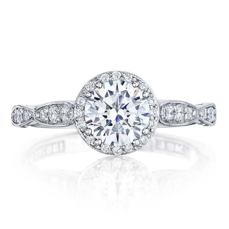 The Tacori Dantela 18K White Gold Round Brilliant Semi Mount Engagement Ring features a breathtaking centerpiece with a large round diamond surrounded by a radiant halo of smaller diamonds. The band, adorned with elegant diamond accents, is set on an impressive cathedral foundation.
