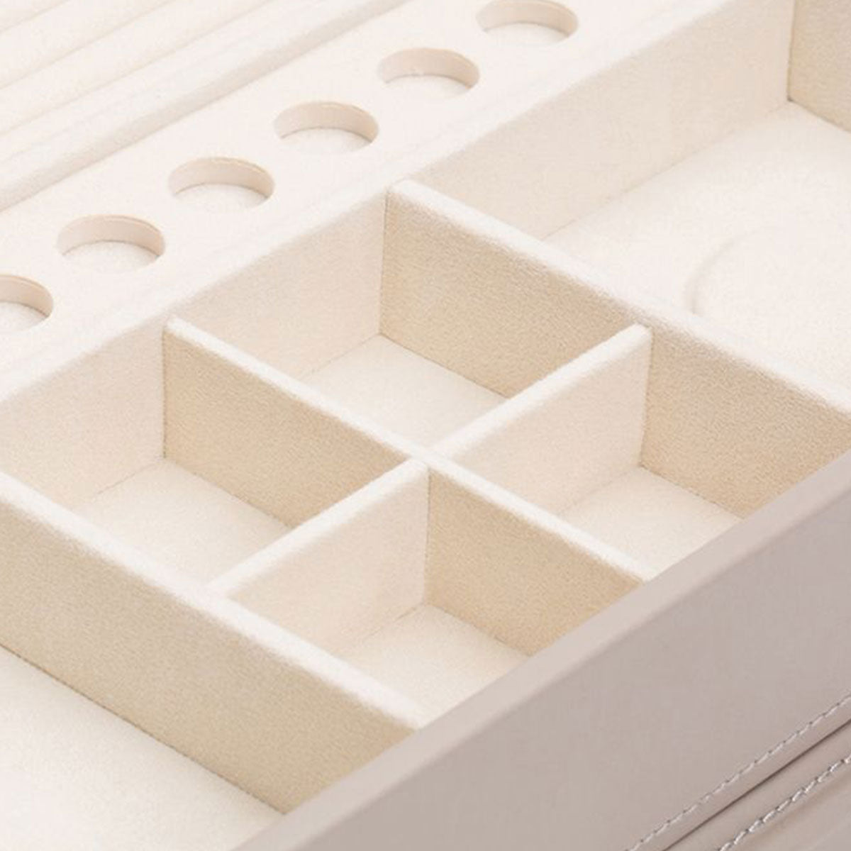 Close-up of a beige WOLF 1834 Jewellery Box with Drawers, crafted from sustainable leather. This organizer features multiple compartments and slots for rings, with an interior lined in LusterLoc anti-tarnish material. It has several square sections and round slots ideal for storing diverse jewelry items.