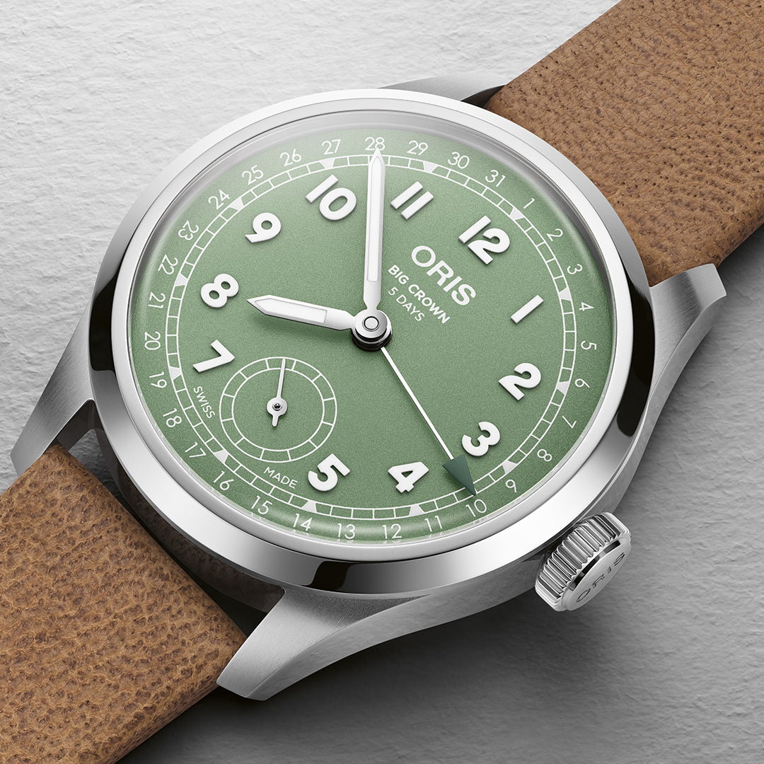 A close-up of the 40mm Oris Big Crown Pointer Date Calibre 403 watch highlights its green dial with Arabic numerals, date indicator, and small seconds subdial at 6 o'clock. This Swiss design has a silver bezel, tan leather strap, and displays "Oris" and "Big Crown" along with the Calibre 403 on the dial.