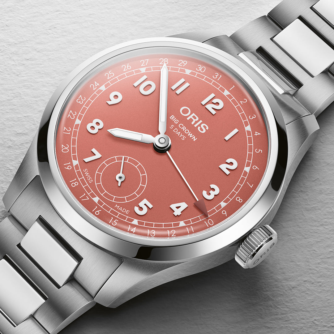 A close-up of the ORIS watch, Big Crown Pointer Date Calibre 403 Automatic Winding 40mm, highlights its silver case and salmon-pink dial with white Arabic numerals. Featuring a small seconds subdial at 6 o'clock, it's encased in stainless steel and includes a robust bracelet.
