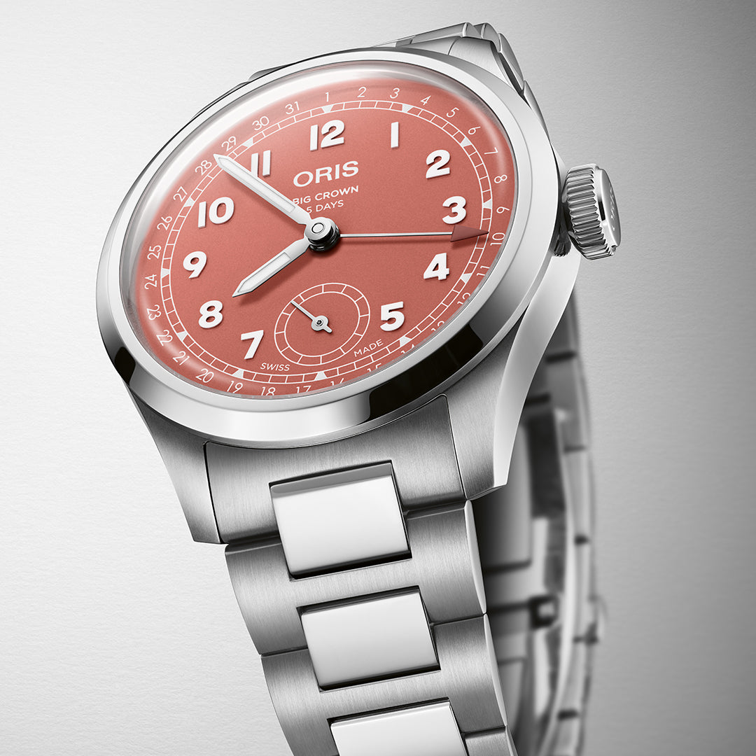 The ORIS Big Crown Pointer Date 40mm watch features a salmon pink dial with Arabic numerals, three hands, and a date subdial at six o'clock. Powered by the Calibre 403 automatic movement, it boasts a stainless steel bezel and bracelet against its neutral backdrop for a sleek look.