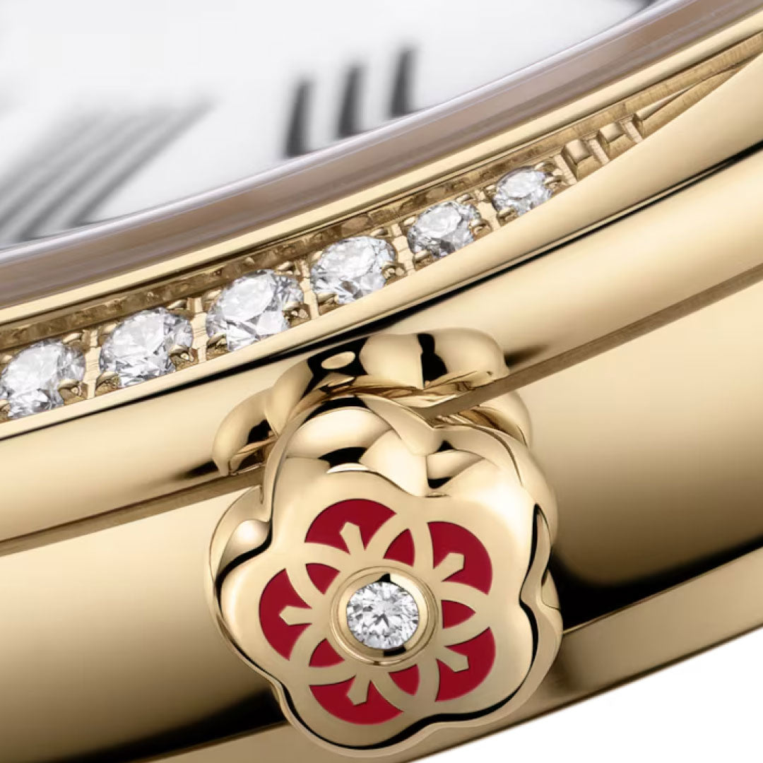 Close-up of the OMEGA De Ville Mini Tresor Quartz 26mm watch case, featuring a red and gold floral crown set with a diamond and a line of small diamonds under the face. Roman numerals are subtly visible on the dial.