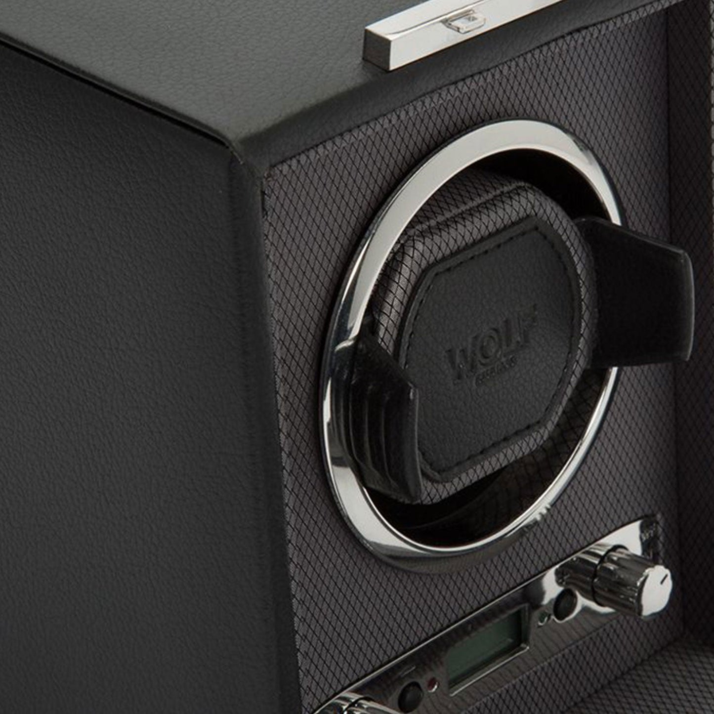 A close-up of the WOLF 1834 Viceroy Black Watch Winder showcases its textured surface. Featuring the "WOLF" brand name, it includes a circular opening with an elegant watch holder encircled by a chrome ring. Below, control knobs and a small digital display make this accessory indispensable for timepiece enthusiasts.