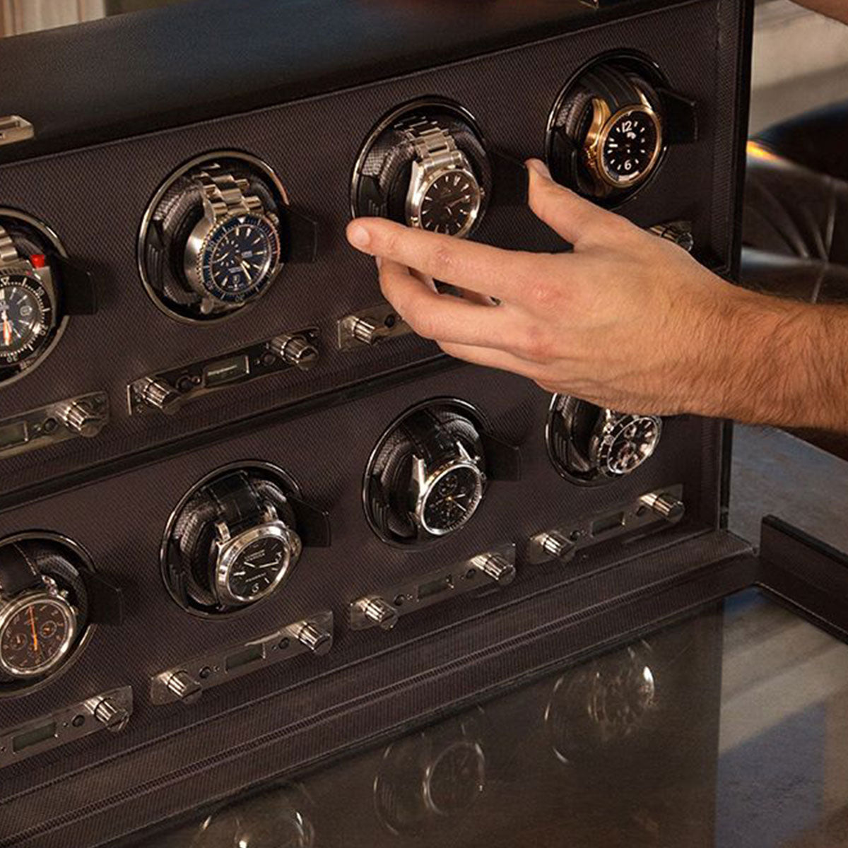 A person adjusts a WOLF 1834 Viceroy Black 8 PCS Watch Winder inside a sophisticated display case. The case accommodates multiple wristwatches in dedicated compartments, each featuring a precise winding mechanism for ultimate accuracy and timeless elegance.