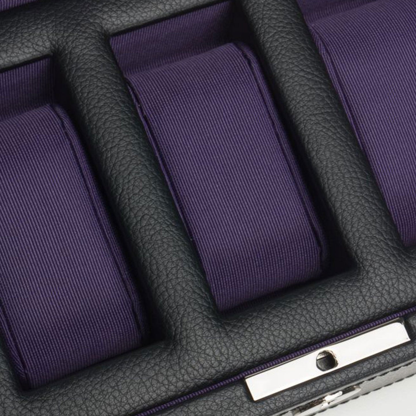 A close-up of the WOLF 1834 Windsor 5 Piece Watch Box showcases its vegan leather exterior and three compartments, each lined with purple fabric to securely hold a watch. This elegant storage solution by WOLF features a silver lock mechanism at the bottom for safe and stylish watch protection.