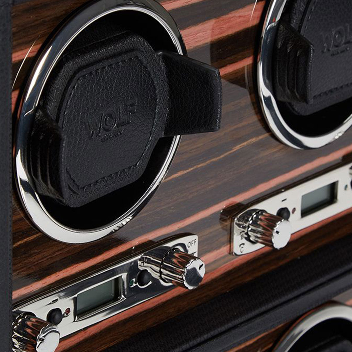 Close-up of the WOLF 1834 Roadster 6 Piece Winder, featuring an ebony macassar wood finish and chrome-finished hardware. This product offers adjustable settings with sleek control knobs and leather cushions to securely hold watches.
