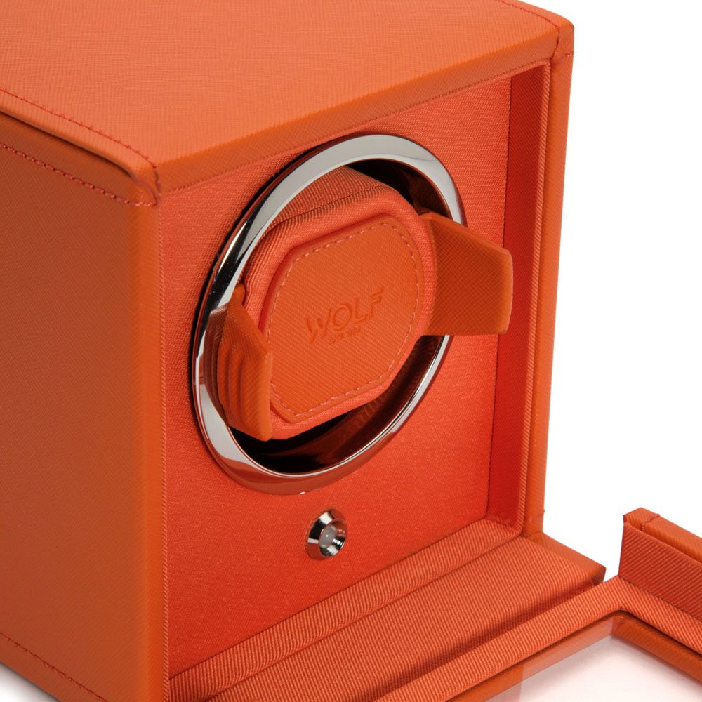 Close-up of the WOLF 1834 Cub Single Watch Winder in orange by WOLF, featuring chrome accents, a vegan leather finish, open box displaying interior, watch holder mechanism, and patented rotation programs.