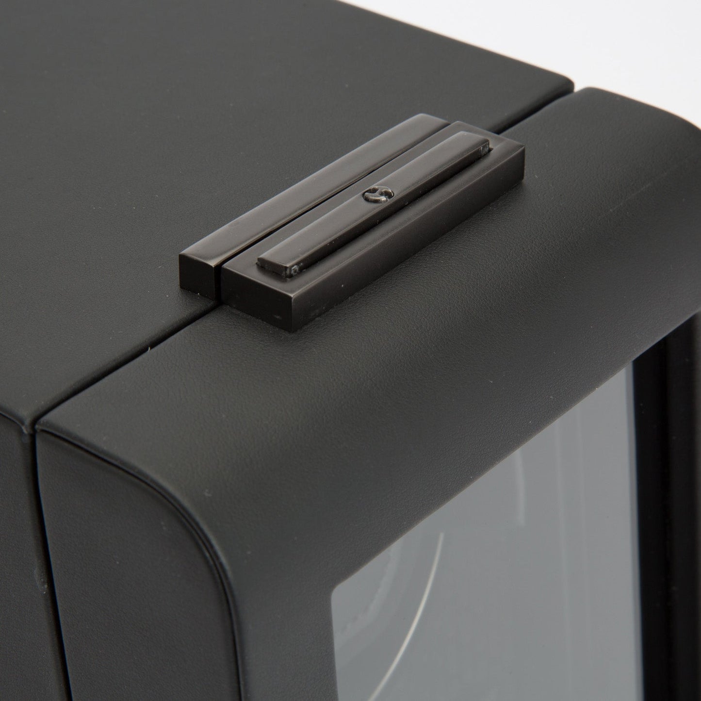 A detailed view of a black WOLF 1834 Axis Single Watch Winder highlighting the top corner, emphasizing the hinge and part of the metal casing, with a textured finish that echoes WOLF's renowned precision.