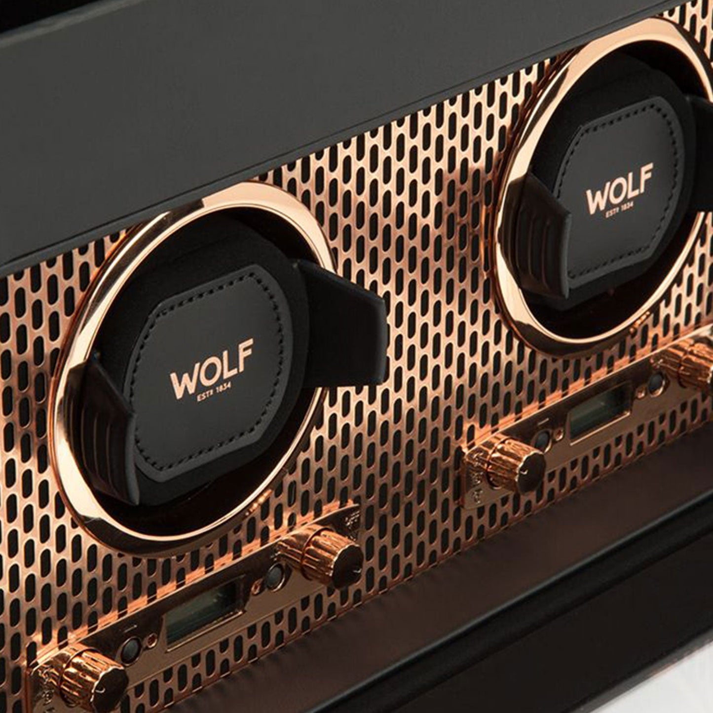 Close-up of the WOLF 1834 Axis Double Winder With Storage, showcasing its luxurious design. The watch winder, with two slots labeled "WOLF," is set on a metallic textured surface. Gold accents and intricate detailing highlight the elegance and sophistication of this copper-plated steel creation in watch storage.