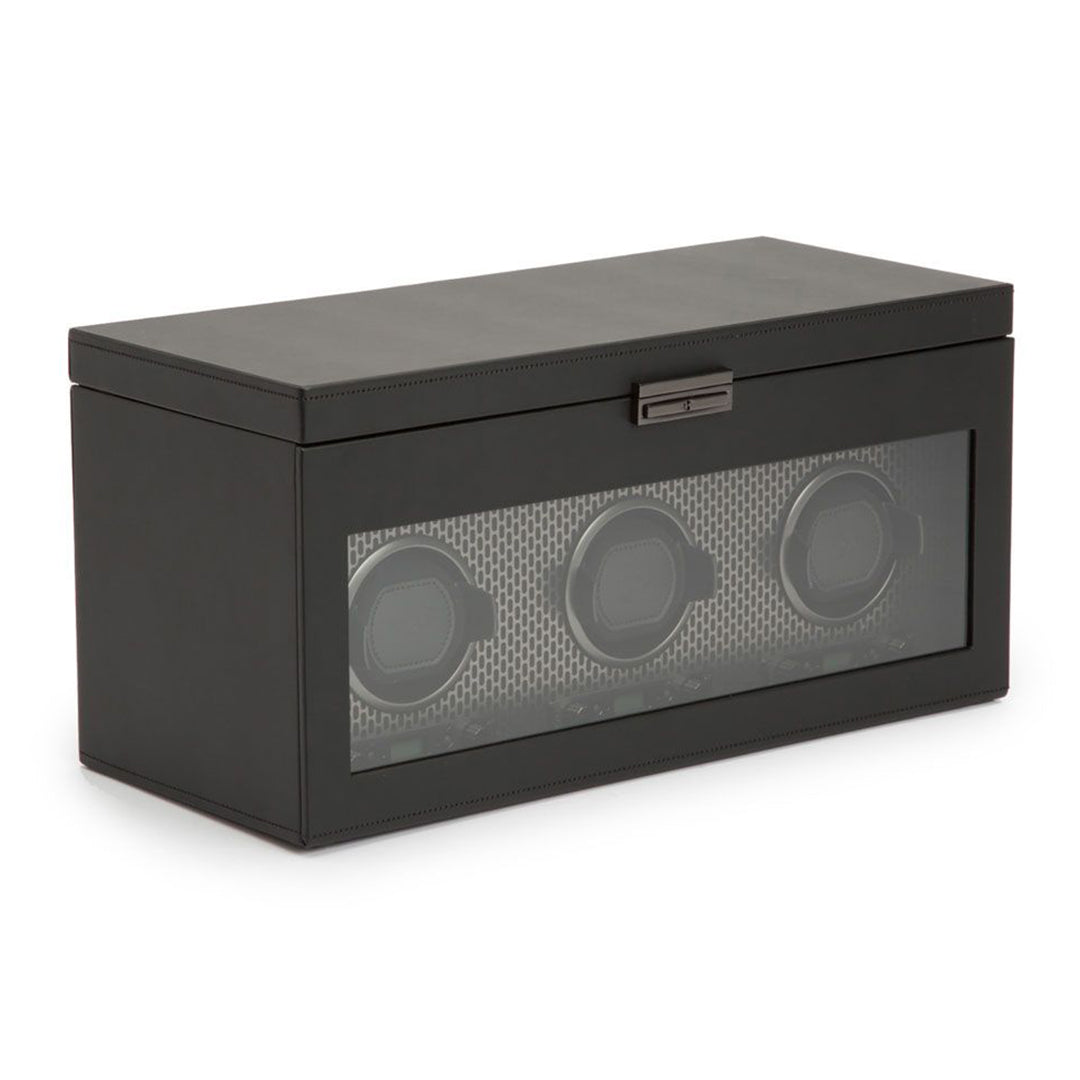 The WOLF 1834 Axis Triple Watch Winder With Storage is a sophisticated black box made from sleek vegan leather and features a glass front showcasing three circular slots for watches. It includes a metallic latch on top and provides multiple rotation options to ensure optimal care for your timepieces.