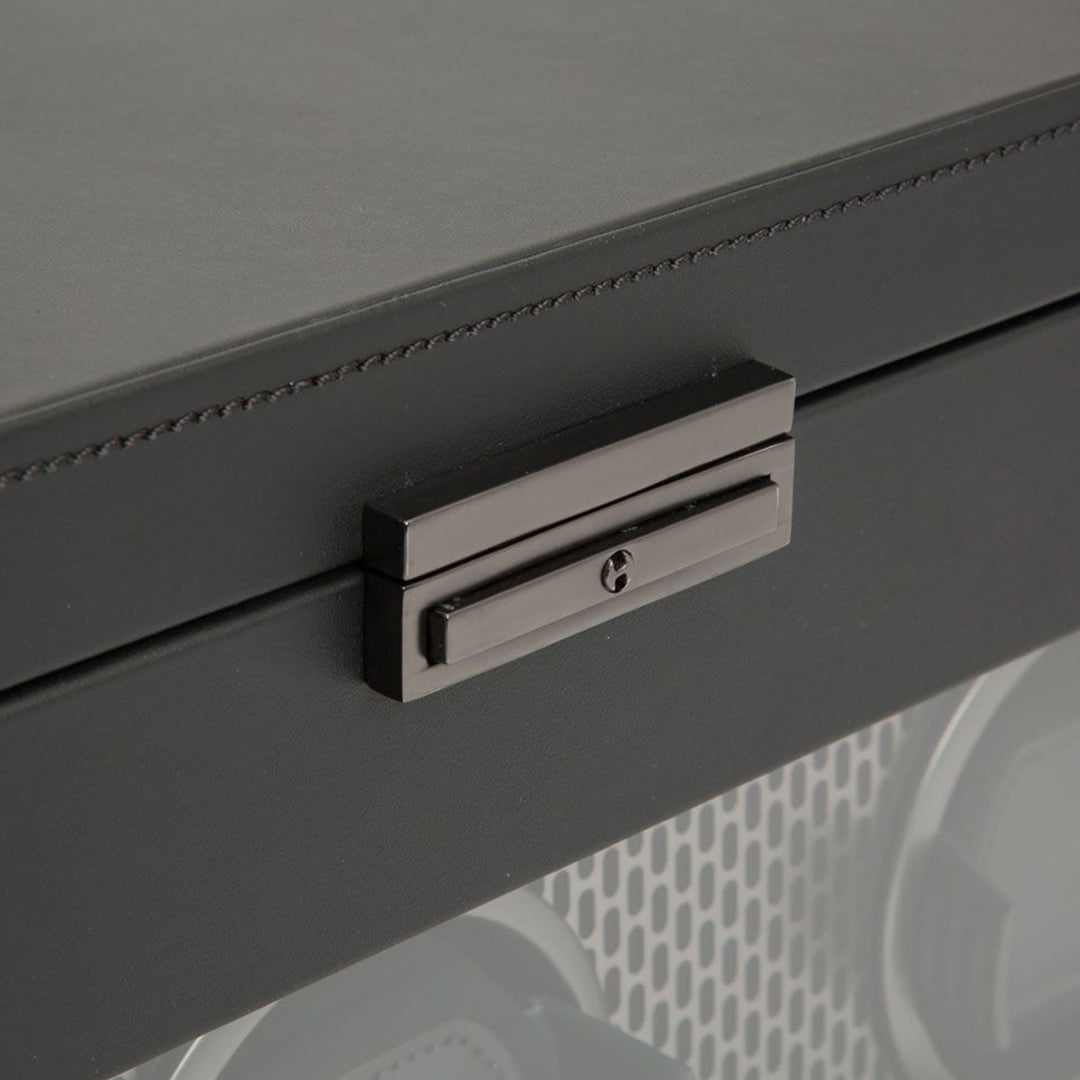 A close-up of the WOLF 1834 Axis Triple Watch Winder With Storage reveals its sleek black leather design, akin to a sophisticated watch winder. It features a dark metallic latch on the front, embodying a modern and minimalistic style. The smooth texture and subtle stitching around the edges further enhance its elegance.