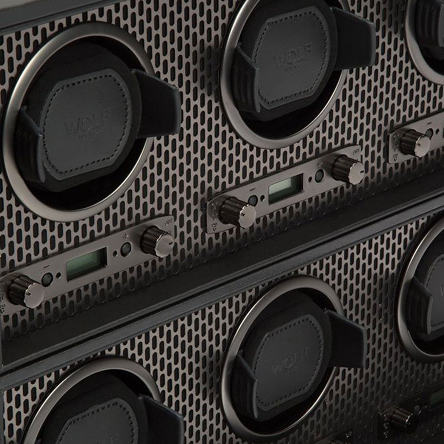 Close-up of the WOLF 1834 Axis Watch Winder, boasting a geometric metal panel adorned with round black components and metal dials. This setup, enhanced with contemporary luxury design elements and digital displays, exudes a sleek, industrial aesthetic.