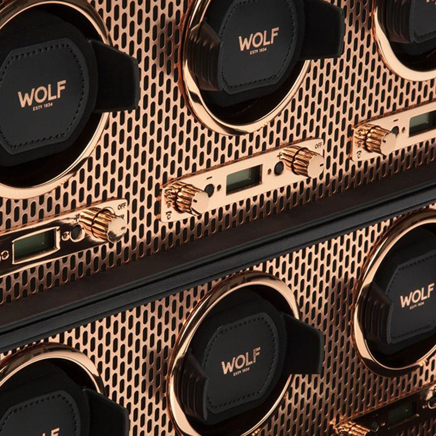 Featuring a detailed view of the WOLF 1834 Axis 6 Piece Winder, this luxurious watch winder panel showcases a sophisticated mesh design. The winders, adorned with gold accents and digital displays alongside control knobs, are elegantly finished in copper and proudly bear the WOLF brand name.
