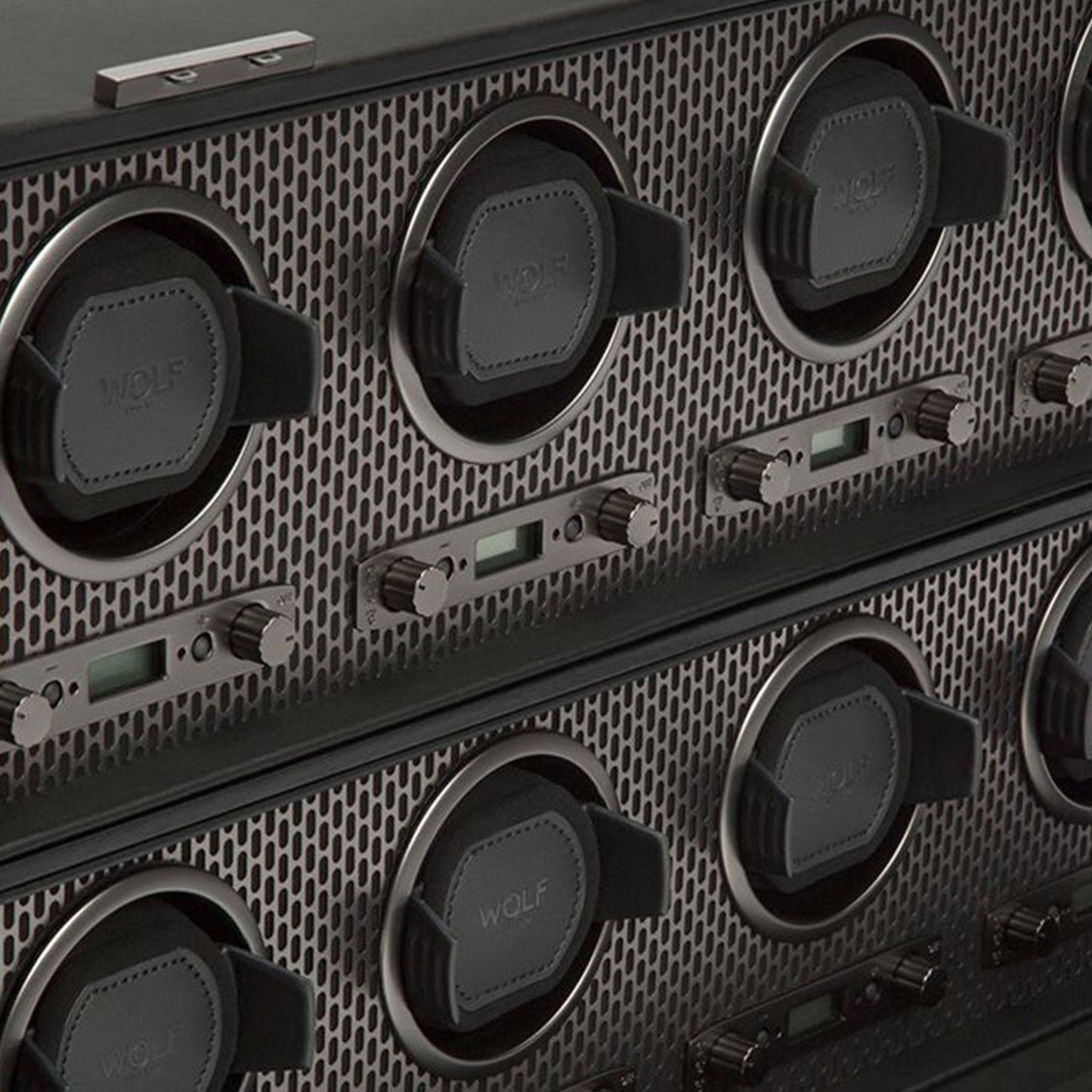 Close-up of the WOLF 1834 Axis 8 Piece Winder, showcasing patented technology for flawless timepiece rotation. This exquisite design features multiple circular slots with leather cushions and adjustable controls, all set within a sleek metallic mesh background.