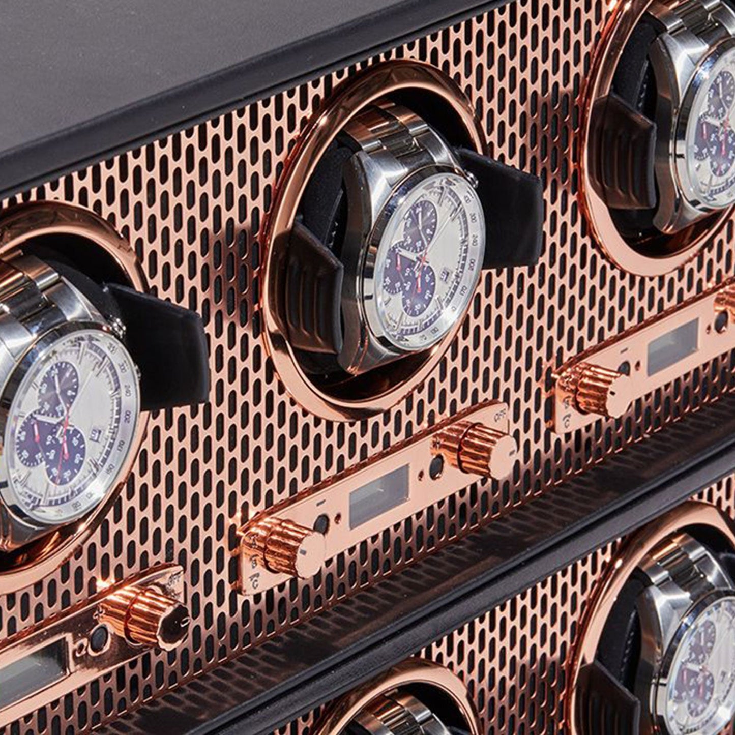 Close-up of the WOLF 1834 Axis 8 Piece Winder elegantly displaying several silver and black watches with detailed dials. This sophisticated winder from WOLF features a rose gold mesh design accented with metallic knobs and patented technology, offering multiple compartments to beautifully showcase your collection.