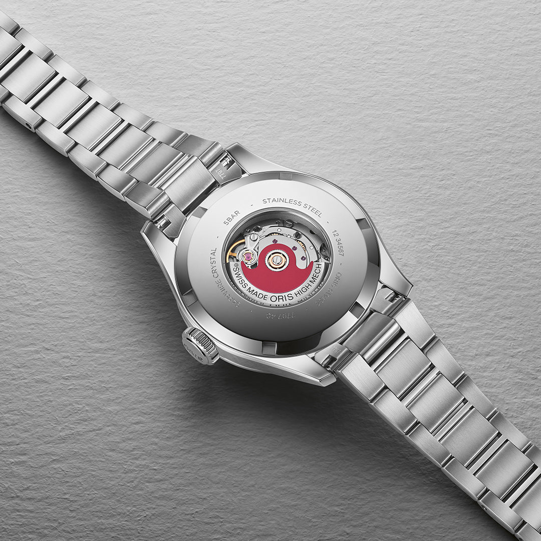 Close-up of the ORIS Big Crown Calibre 531 Automatic Winding 34mm Swiss Made watch, ideal for smaller wrists. It features a visible mechanical movement, a transparent case with intricate gears and red accents, plus a polished link bracelet against a textured grey background.