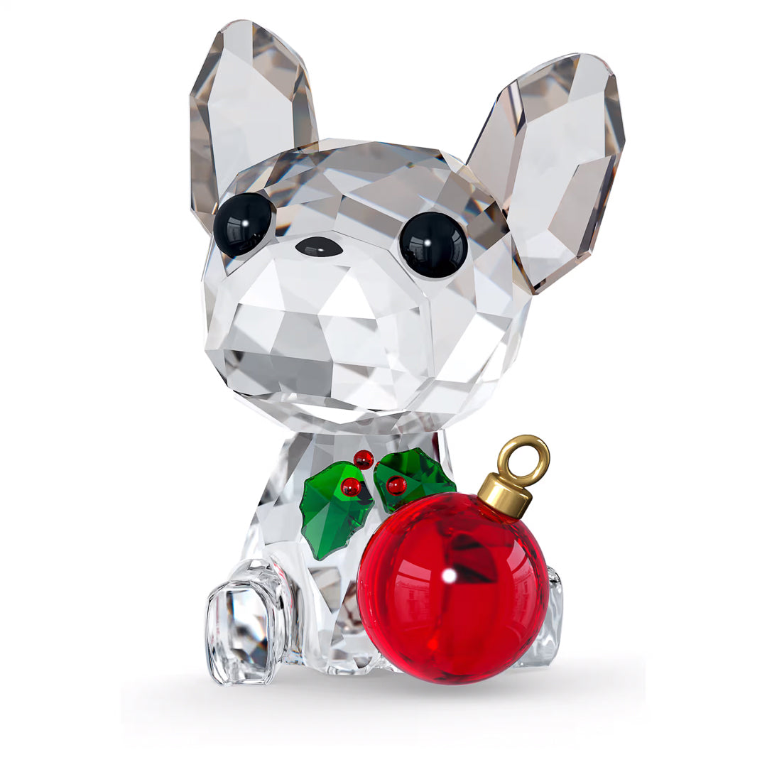 The Swarovski Holiday Cheers French Bulldog Home Décor piece beautifully embodies the holiday spirit, featuring large black eyes. This charming figurine is adorned with green holly and red berries around its neck and holds a shiny red Christmas ornament, with its faceted design reflecting light magnificently.