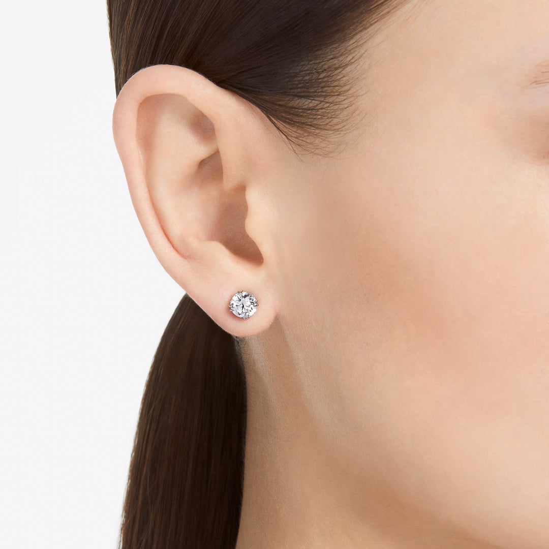 Close-up of a person's ear adorned with the sophisticated Swarovski Stilla Stud Earring, featuring diamond-like zirconia. The brown hair is tied back, accentuating the rhodium-plated earring against the plain white background.
