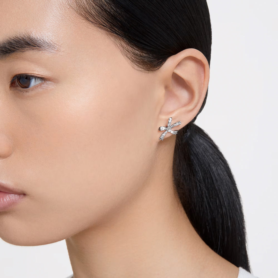 Close-up of a person with long black hair wearing Swarovski Hyperbola Stud Earrings, known for their exquisite shine. The pristine white background enhances the focus on the Swarovski jewelry and the individual's profile.