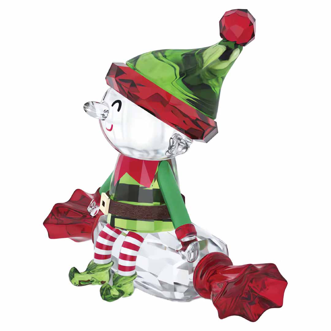 The Swarovski Holiday Cheers Dulcis Elf Home Décor features a sparkling crystal figurine of a festive elf adorned in a vibrant green and red hat, perched atop a crystal candy. This charming holiday piece captures the joy of the season with the elf's striped red and white stockings, green outfit, and delightful smile as he holds a red bag in each hand.