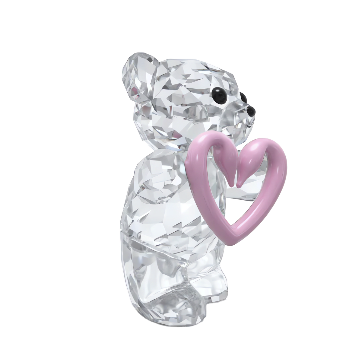 A faceted Swarovski Kris Bear Una Bear Style Number figurine by Swarovski, featuring black eyes, holds a shiny pink heart in its paws against a plain white background.