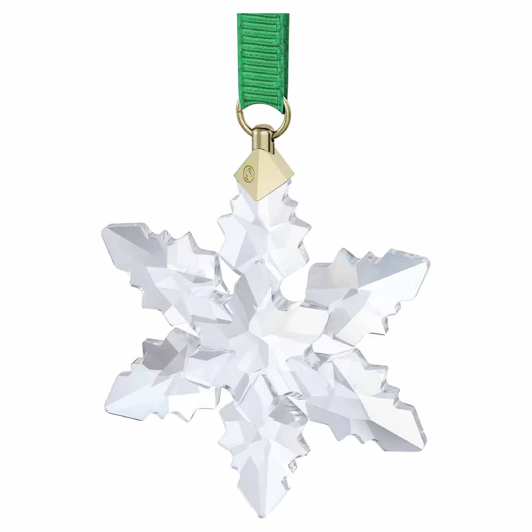 A Swarovski 2024 Annual Edition Ornament Set Home Décor piece, featuring intricate facets, hangs elegantly from a green ribbon. This Swarovski ornament beautifully reflects light, adding a festive touch to any snowflake decoration collection.