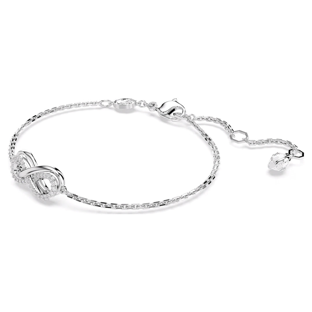 The Swarovski Hyperbola Bracelet showcases an elegant silver design with a textured knot in the center, complemented by an adjustable chain and clasp. Its infinity motif imparts a delicate and sophisticated charm against a white background.