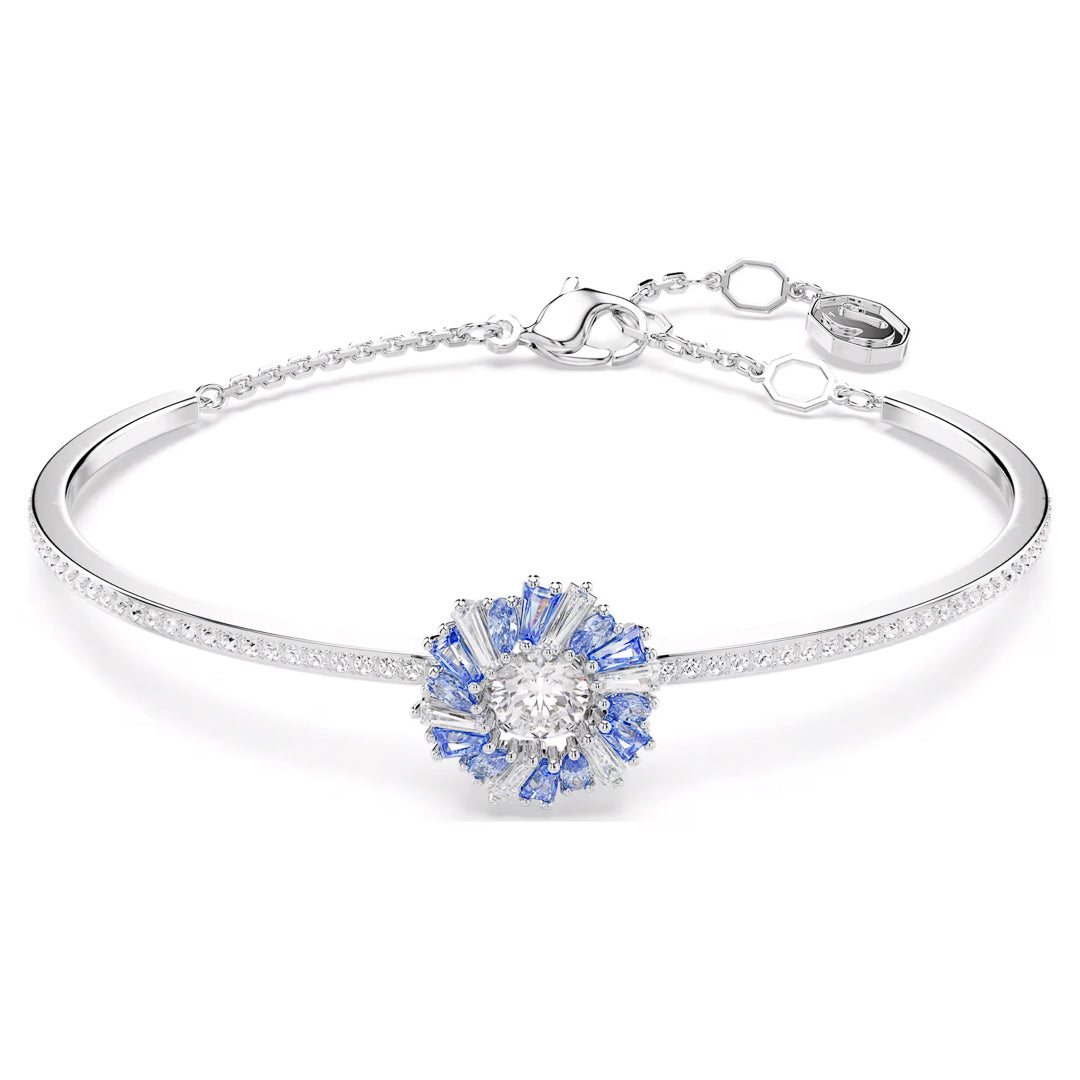 This exquisite Swarovski Idyllia Bangle echoes the elegance of a rhodium-plated silver bracelet with its floral design, adorned with blue and clear gemstones at the center. It includes an adjustable chain, a clasp closure, and a small engraved tag.