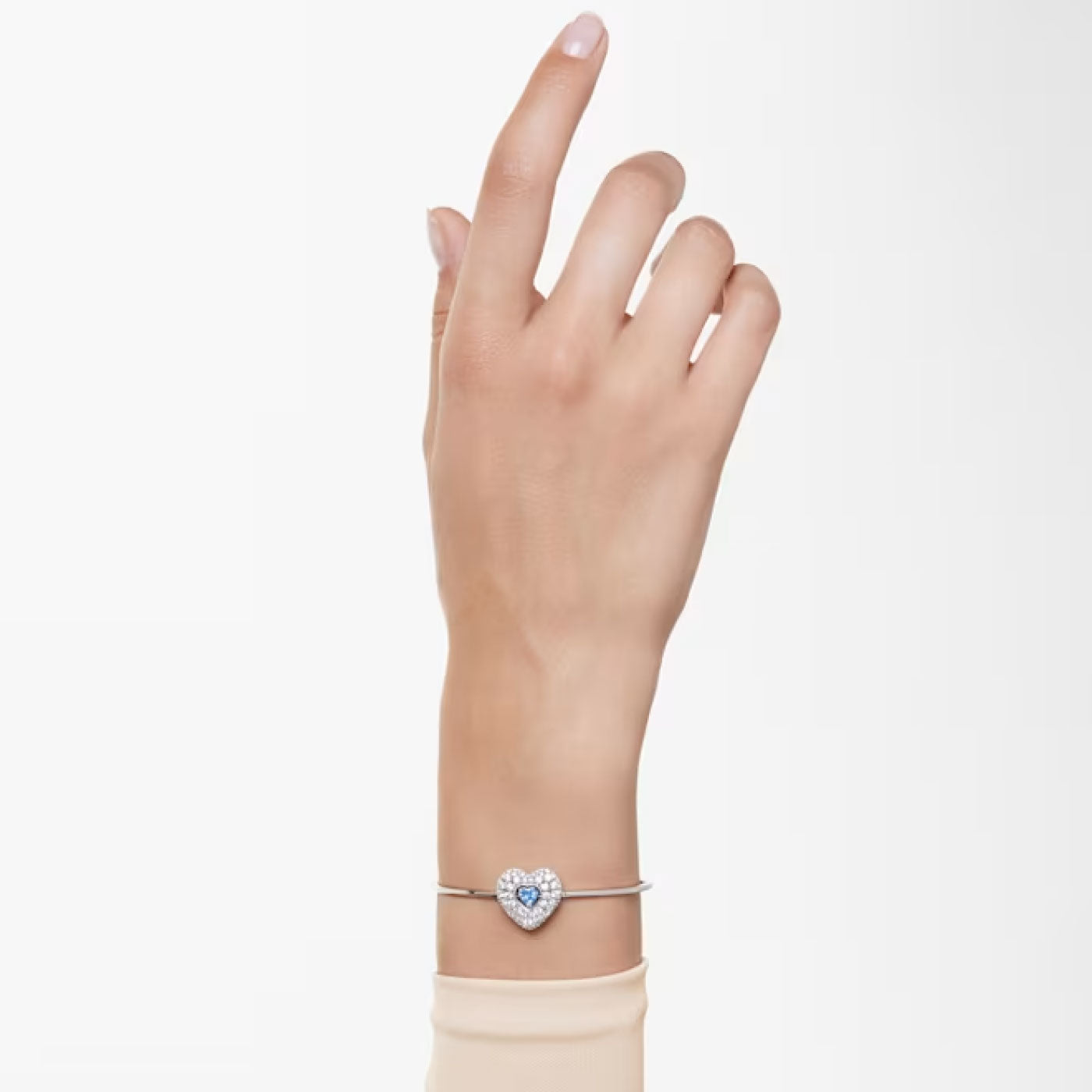 A hand with a polished pink manicure wears an elegant bracelet, the Swarovski Hyperbola Heart Bangle, featuring a heart-shaped charm adorned with Swarovski's signature Zirconia that twinkle like dancing stars. The arm is raised against a plain, light background, highlighting this stunning piece from Swarovski.