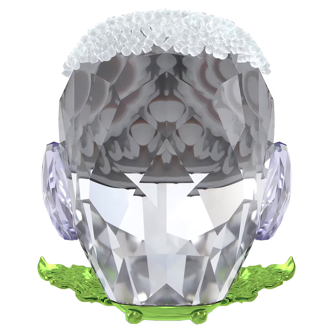 The Swarovski Idyllia Baby Owl Home Décor by Swarovski is a captivating crystal sculpture designed as a stylized head. It showcases a faceted surface and is topped with a textured white section reminiscent of hair, accompanied by lavender ear-like elements that mirror the allure of a baby owl. The piece rests on a green base embellished with leaf-like patterns, enhancing its charm as home décor.