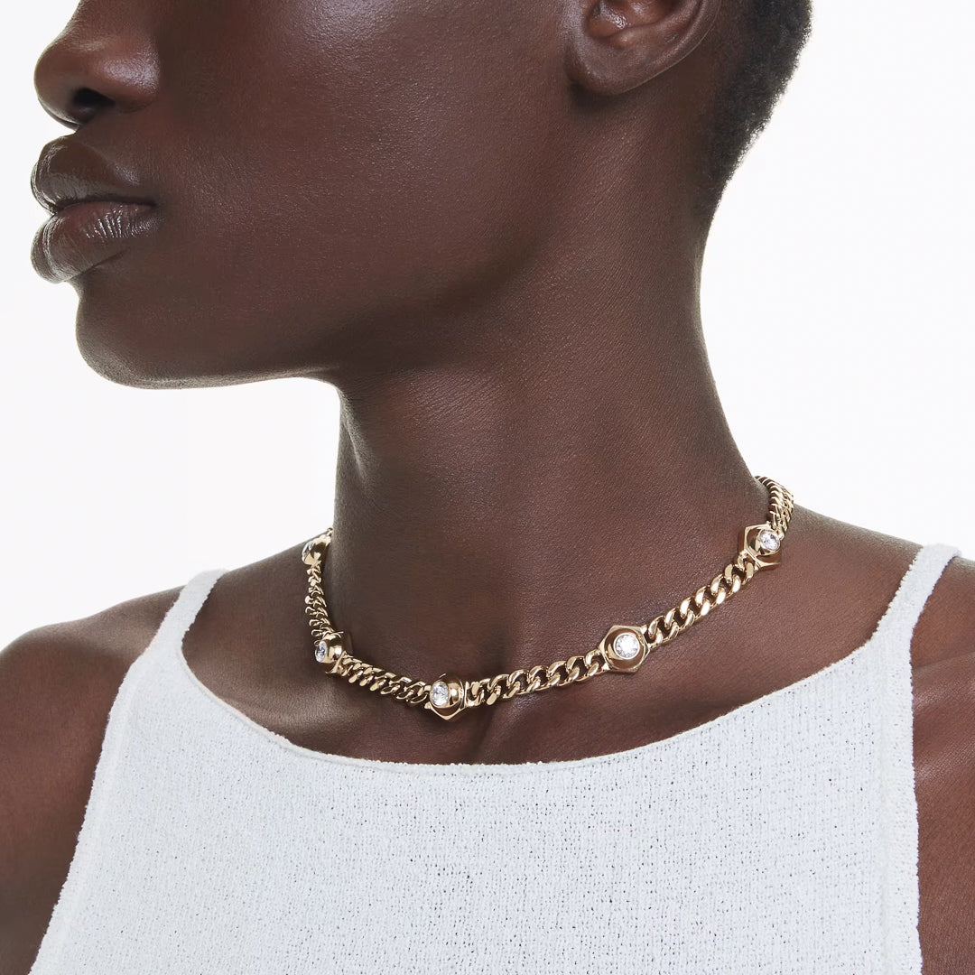 A person wearing the Swarovski Numia Necklace, a stunning piece from Swarovski featuring gold-tone plating with pearl accents and industrial-style elements. The individual is dressed in a white sleeveless top against a plain background.