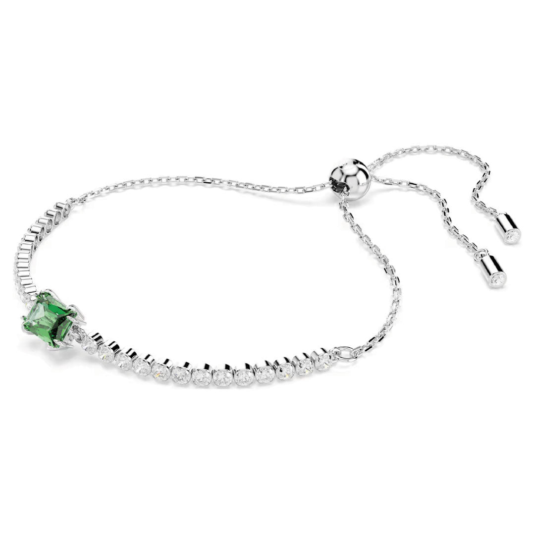 The Swarovski Matrix Tennis Bracelet by Swarovski is a delicate rhodium-plated silver piece featuring a stunning green emerald stone centerpiece, flanked by a line of sparkling diamonds. The adjustable chain, adorned with Swarovski Zirconia capped ends, elegantly secures with a round sliding clasp.