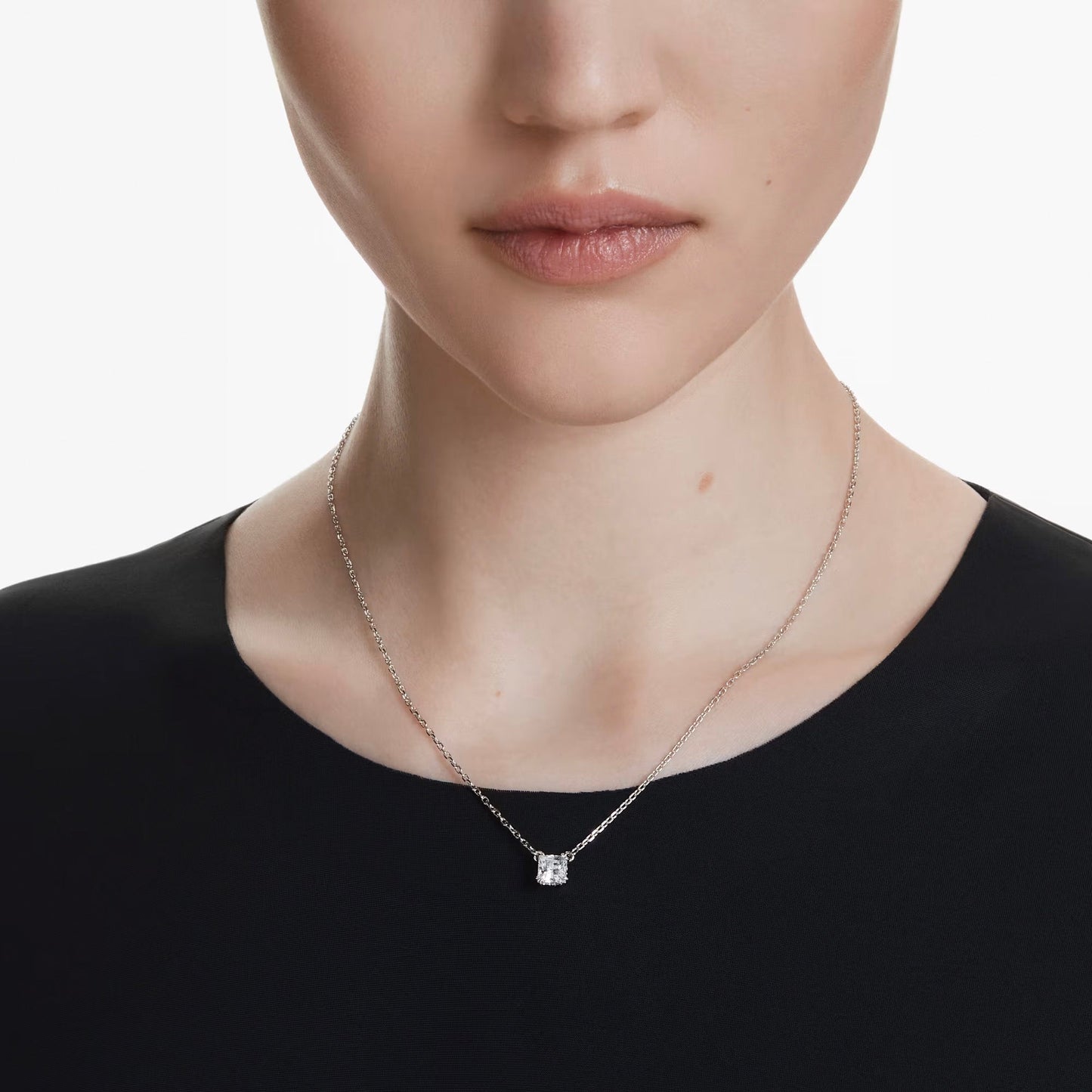 A person adorned with a Swarovski Stilla Attract Square Cut Necklace Pendant on a rhodium-plated silver chain. The individual has short hair and is dressed in a black top, set against a plain white background.