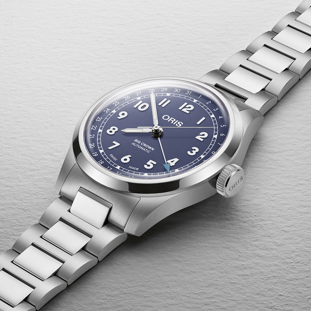 The ORIS Big Crown Pointer Date Calibre 754 Automatic features a blue dial with white numerals and silver hands, complemented by a stainless steel bracelet. It includes a date indicator at 6 o'clock and showcases the brand name below 12 o'clock, enhancing its sleek Swiss Made design.