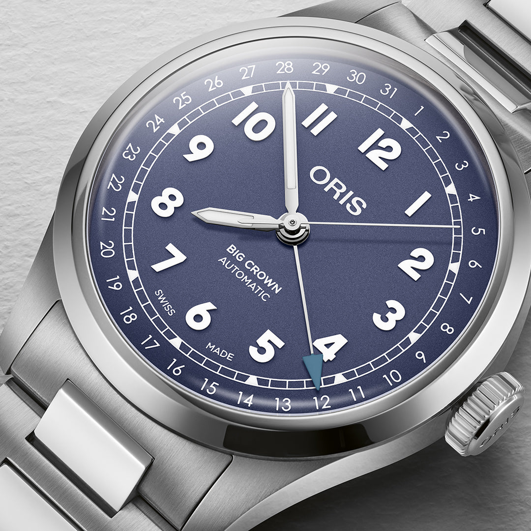 A close-up of the Oris Big Crown Pointer Date Calibre 754 Automatic Winding 40mm Watch features a silver case with a blue dial, white numerals, and date window. The stainless steel bracelet complements its design and automatic movement, prominently labeled "Swiss Made.