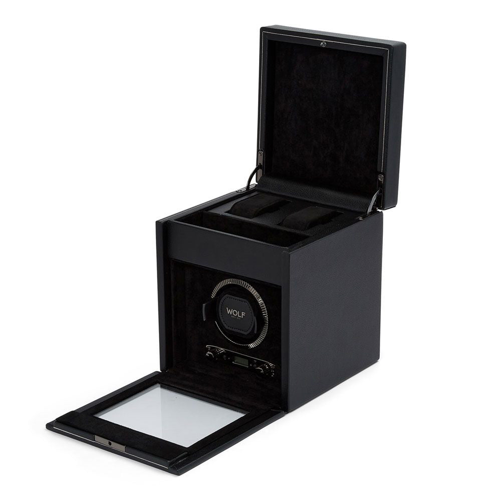 The WOLF 1834 British Racing Watch Winder With Storage is displayed with its lid open. Designed in a square shape, it boasts a transparent door and space to accommodate multiple watches. It offers various rotation options and has a black interior. The visible winder is branded, and the open lid reveals additional storage with a lock-in dynamic cuff.