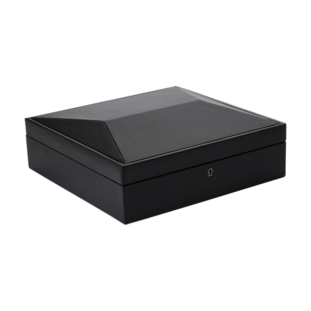 The WOLF 1834 British Racing 15 Piece Watch Box showcases a sophisticated black design made from vegan leather, featuring a stylish angular shape. This square box includes a pointed lid and a small keyhole at the front for secure lock and key closure, elegantly displayed against a plain white background.