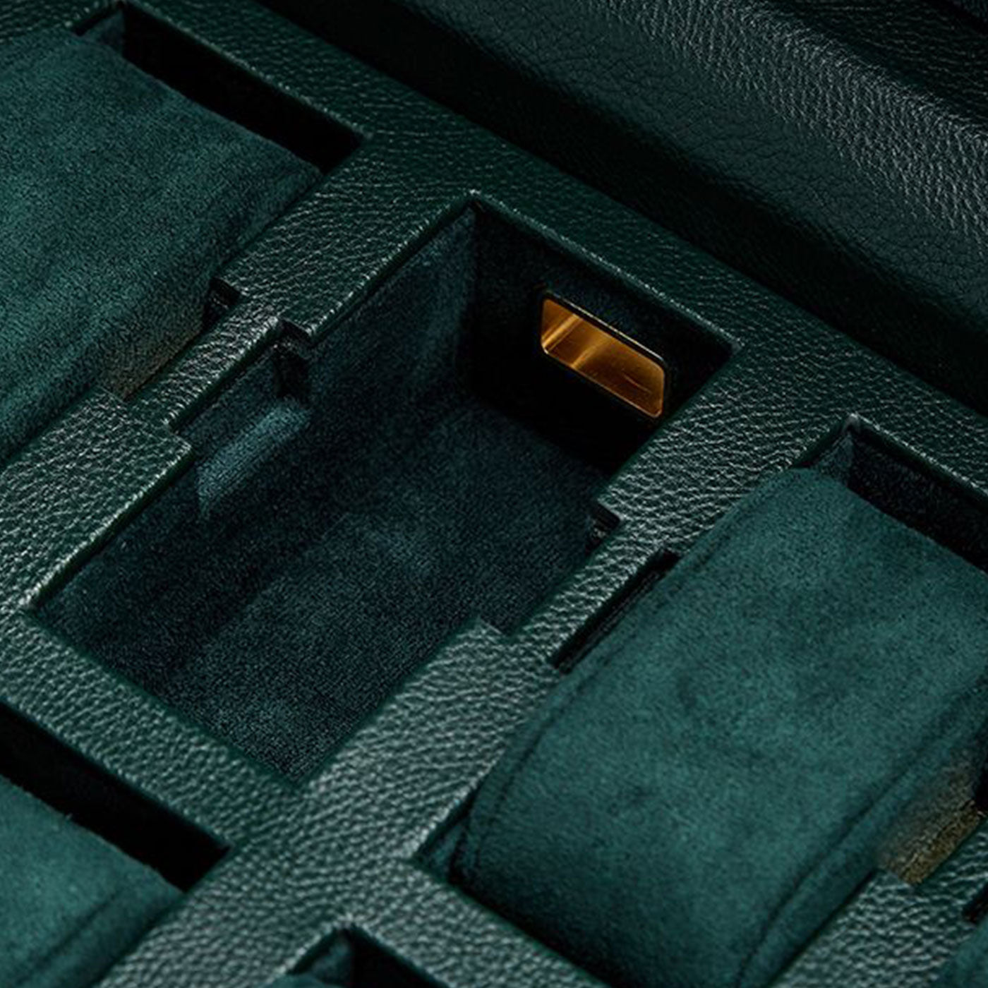Close-up of the WOLF 1834 British Racing 15 Piece Watch Box in dark green vegan leather and suede, featuring empty slots for watch storage. A small gold detail enhances one section, adding a touch of luxury to the interior.