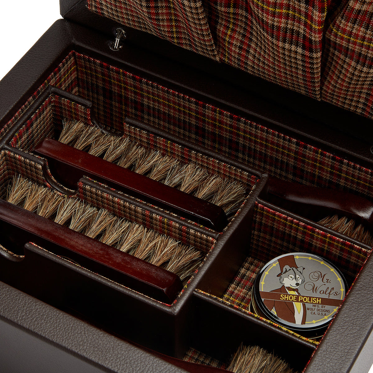 The WOLF 1834 WM Brown Shoe Shine Case includes brushes and a tin of shoe polish labeled "Mr. Wolf's." Its interior showcases a plaid fabric reminiscent of the WM Brown style, while the brushes feature wooden handles with natural bristles.