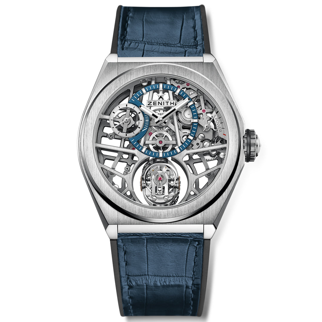 The ZENITH Defy Zero G El Primero 8812 S 44mm Watch flaunts a silver skeleton movement face with visible intricate gears, a blue hour marker ring, and a blue leather strap. The Zenith brand name crowns the top center, highlighting its gyroscopic innovation.