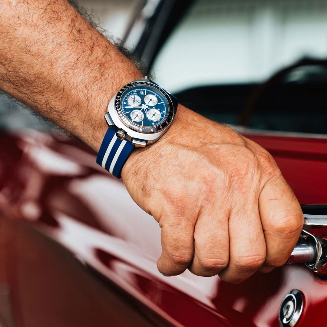 A close-up of a hand wearing the Bulova Shelby Racer Chronograph Quartz 43mm Watch, Limited Edition of 7,500 pieces, while gripping the door handle of a red car.